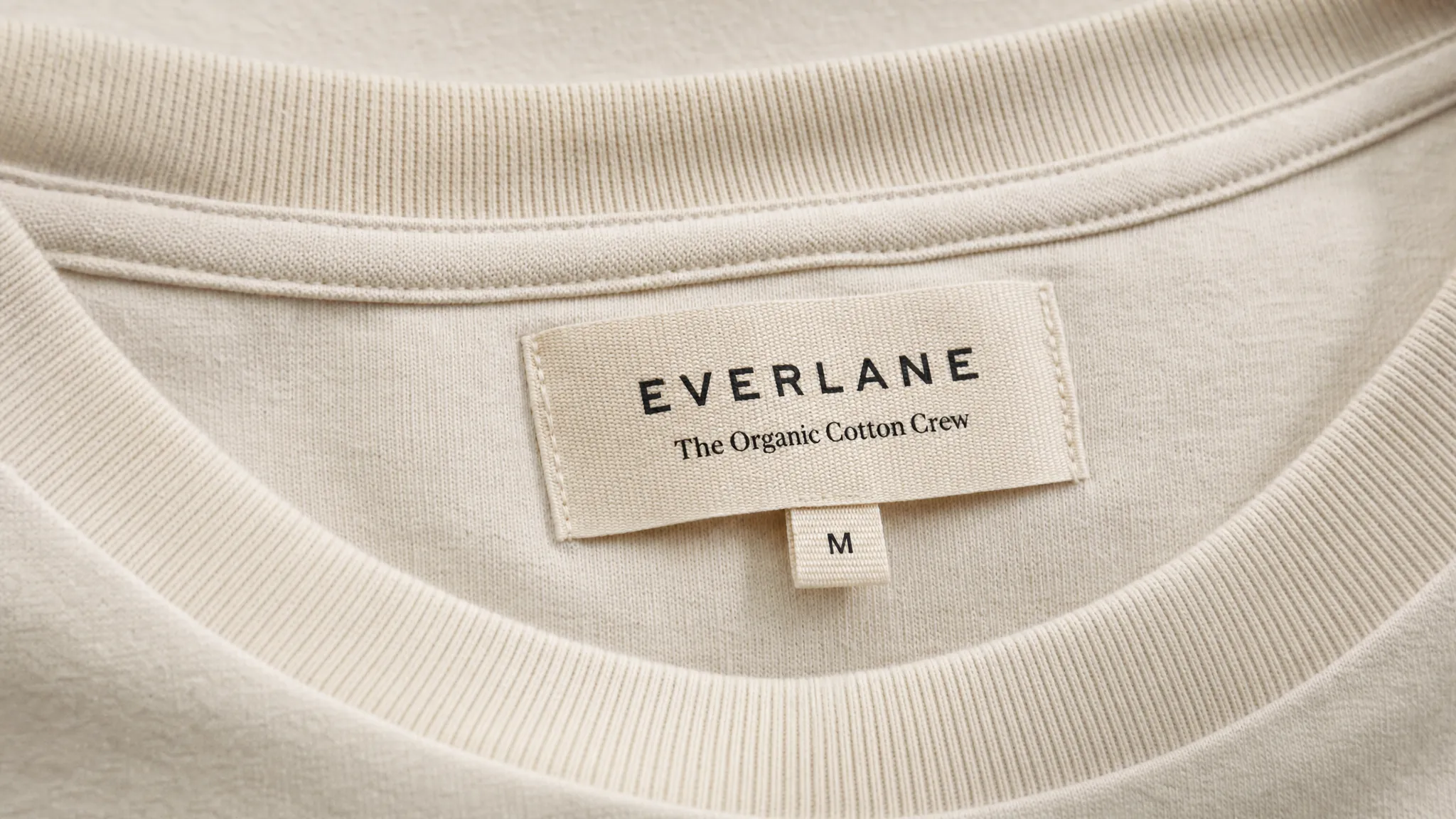 A close-up of premium apparel with a neatly stitched woven brand label, showing fine thread texture, clean typography, and careful placement on soft fabric.