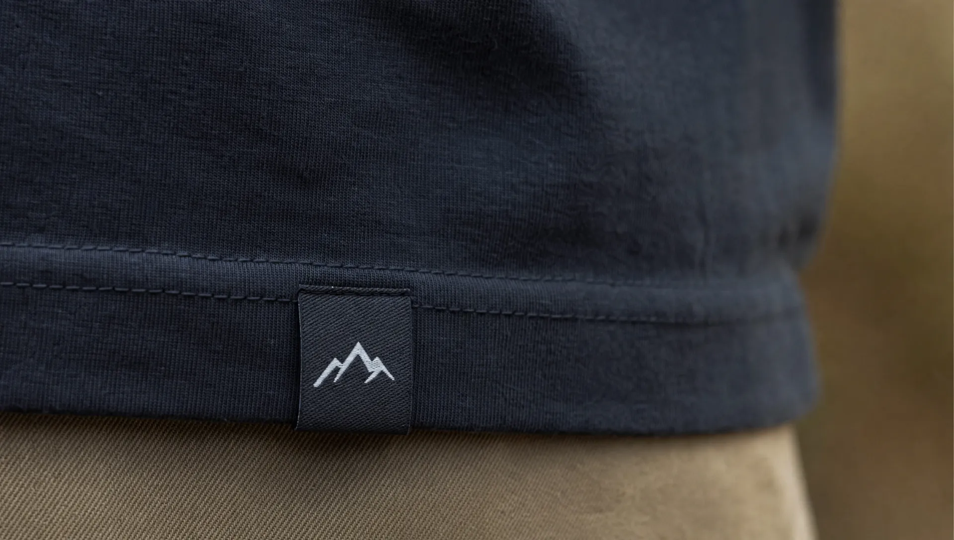 Close-up of a finished garment with a small woven logo label sewn neatly into the hem, showing clean stitching, textured fabric, and a polished brand detail.
