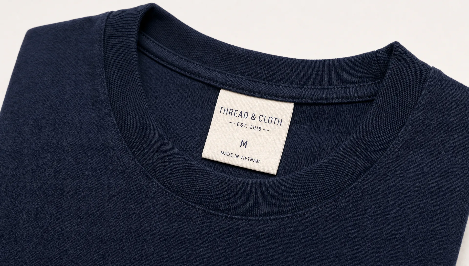 Close-up of a single folded garment with a woven clothing label sewn into the neckline seam, showing clean stitching and readable branding in a simple retail-ready presentation.