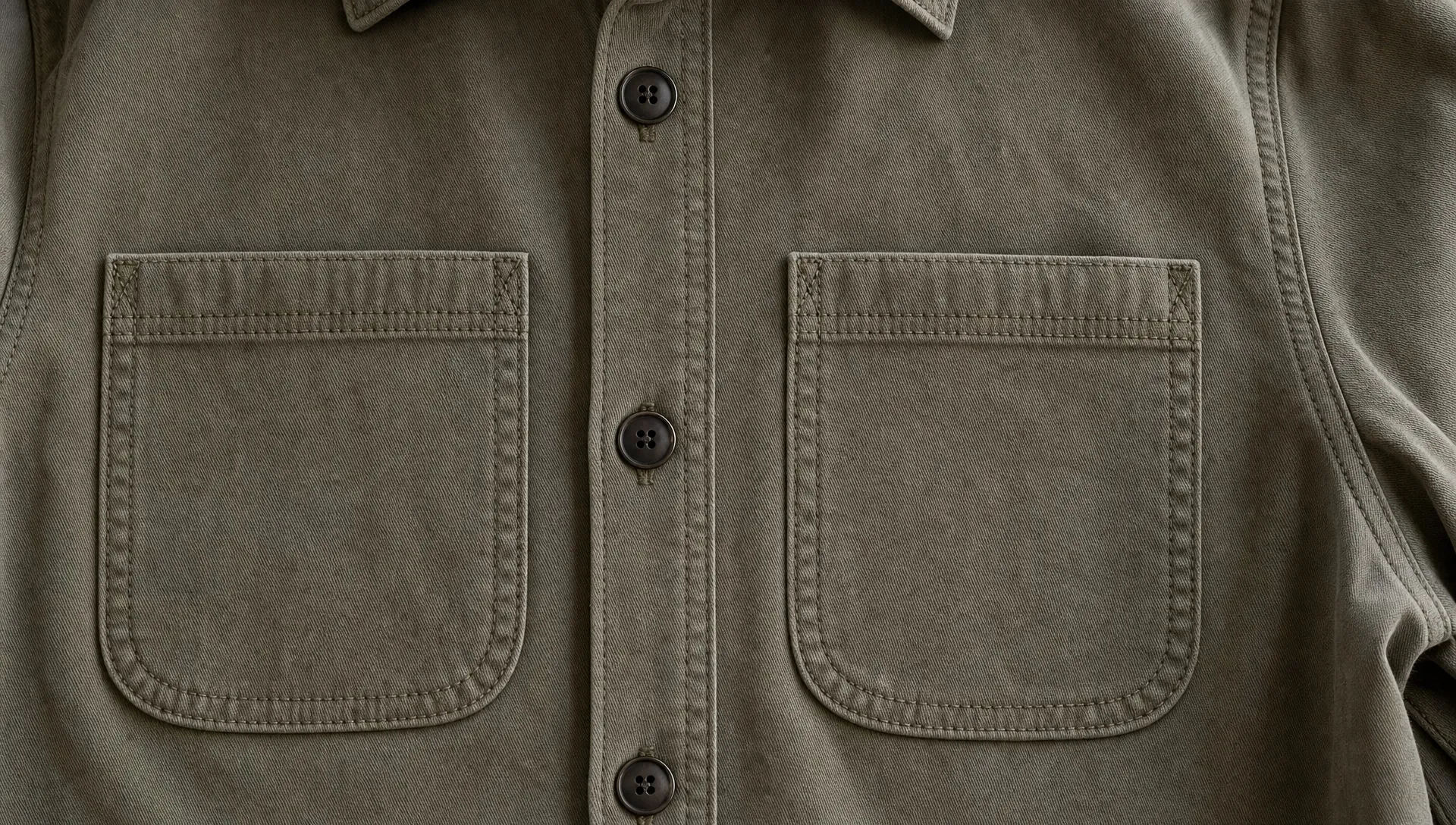 Close-up of a structured overshirt with two patch pockets, rounded lower corners, reinforced upper corners, and visible topstitching.
