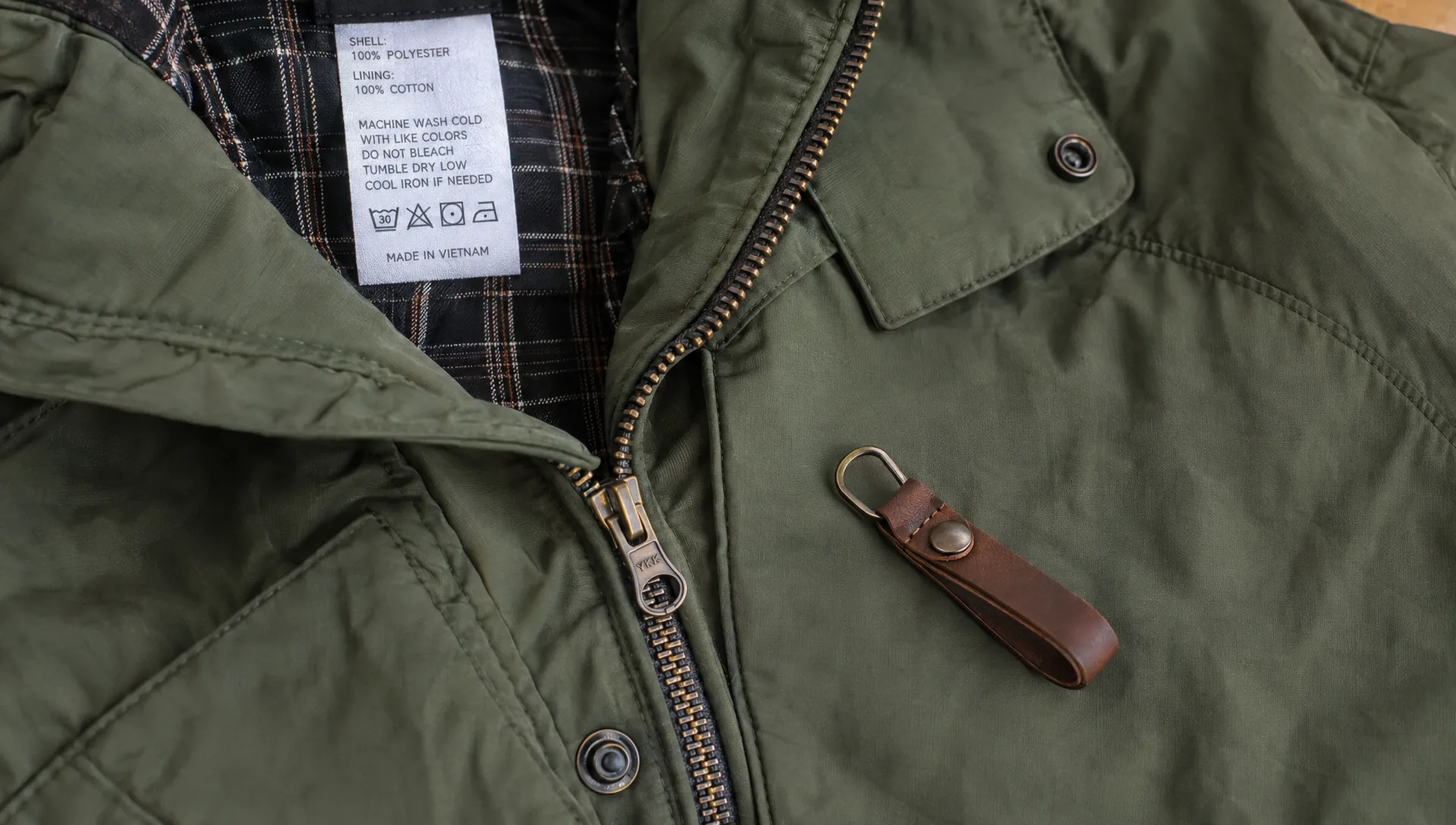 A washable jacket lies flat with its care label visible, while a leather detachable pull rests beside the zipper whose original metal tab remains attached.