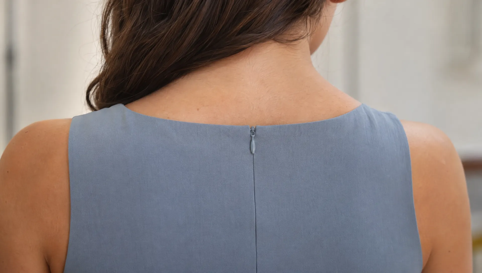 At the back neckline of a dress on a wearer, the closed invisible zipper’s tonal tab rests along the aligned seam.